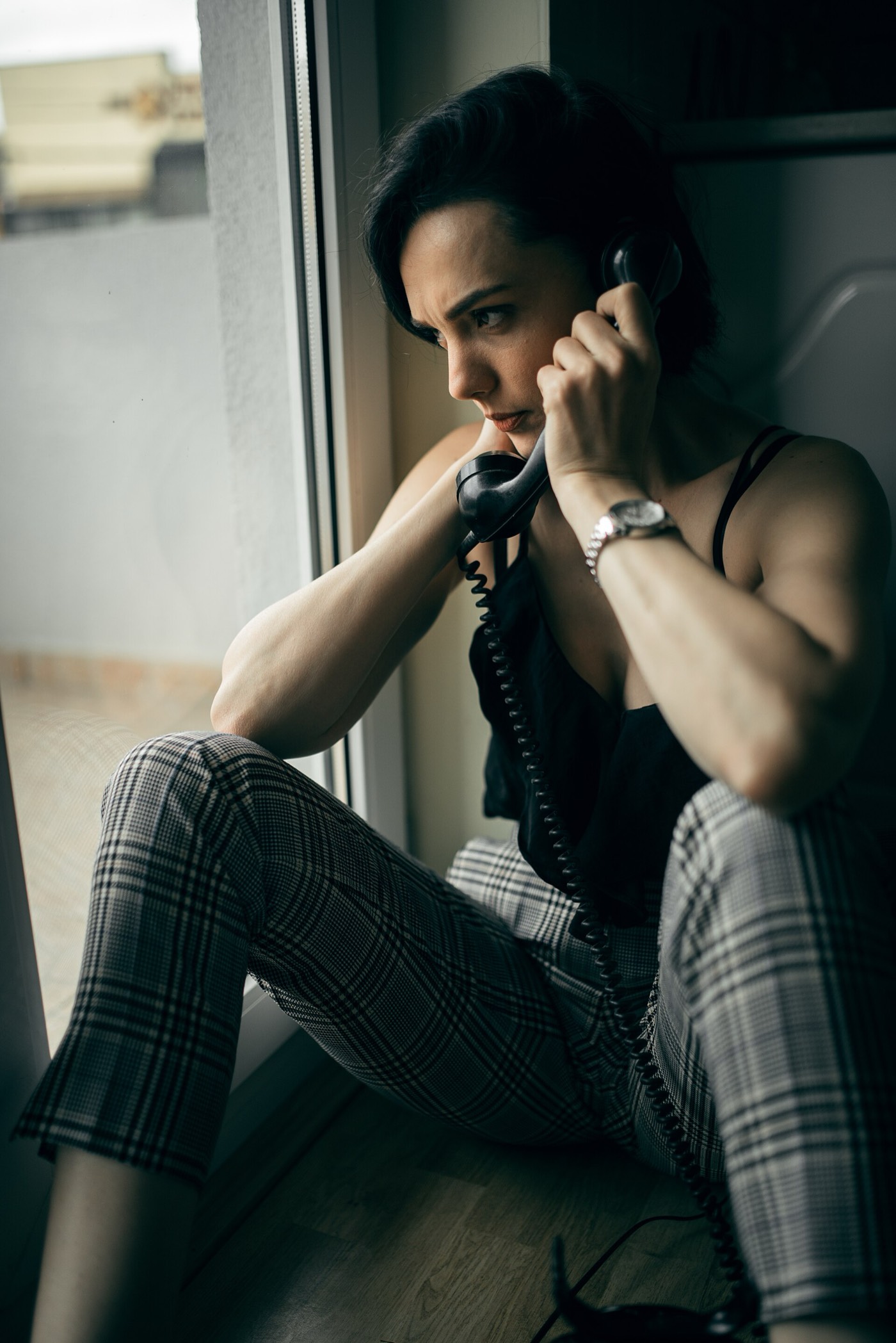 A man at a window, phone to his ear, thinking before he answers.