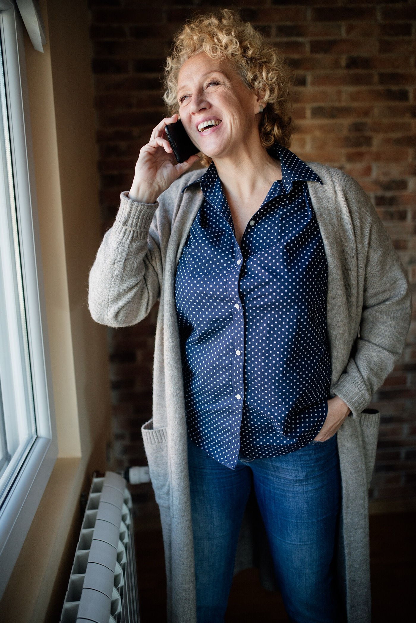A woman laughing on the phone by a bright window.